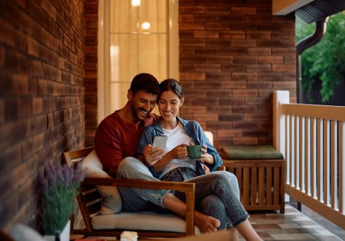 Relaxed couple using mobile phone while spending an afternoon on the porch. Copy space.